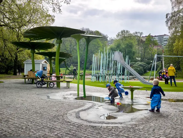 Lekplats i regn med barn som leker i parken och med vattnet.