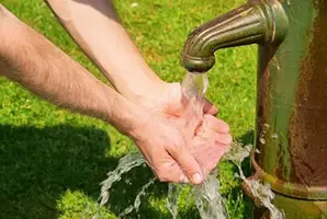Person sköljer händerna i vatten från en brunn.