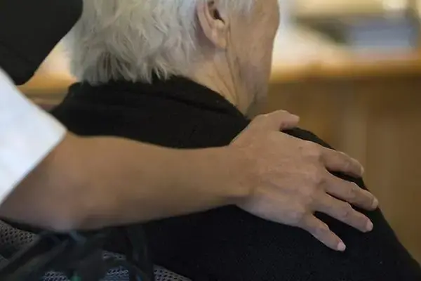 Vårdpersonal håller en öm hand på äldre persons axel.