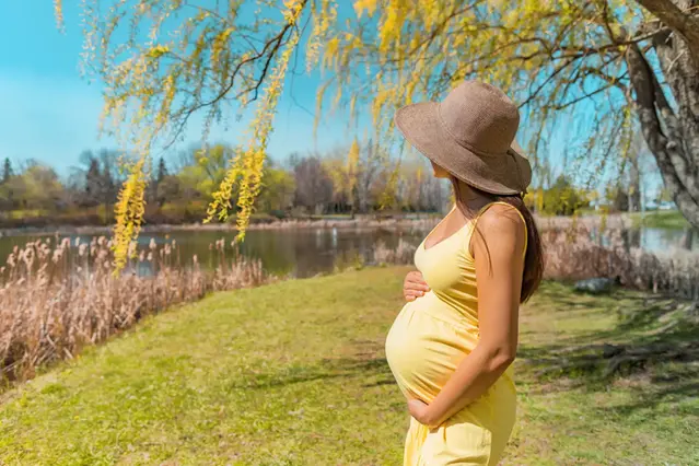 Gravid kvinna med hatt som skydd mot solen, håller om sin mage.