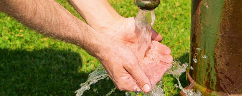 En tvättar händerna under en vattenkran utomhus.