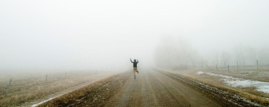 En person springer och skuttar längs en grusväg i dimma.