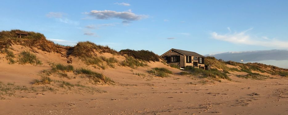 Hus i sanddynelandskap där ena sidan vetter mot öppen strand