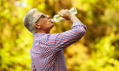 Äldre man dricker vatten ur plastflaska